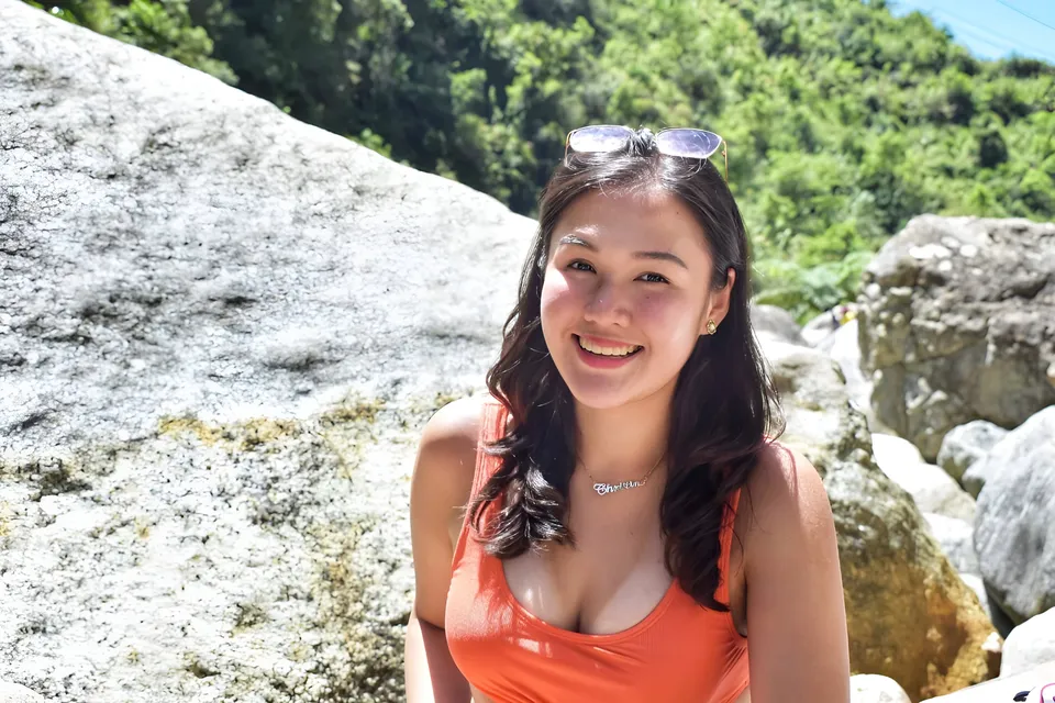 Christine Cabacungan in orange top seated outdoors near large rocks