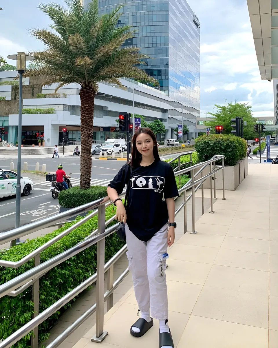 Clairee Winslow in black t-shirt and white pants stands on sidewalk near palm tree
