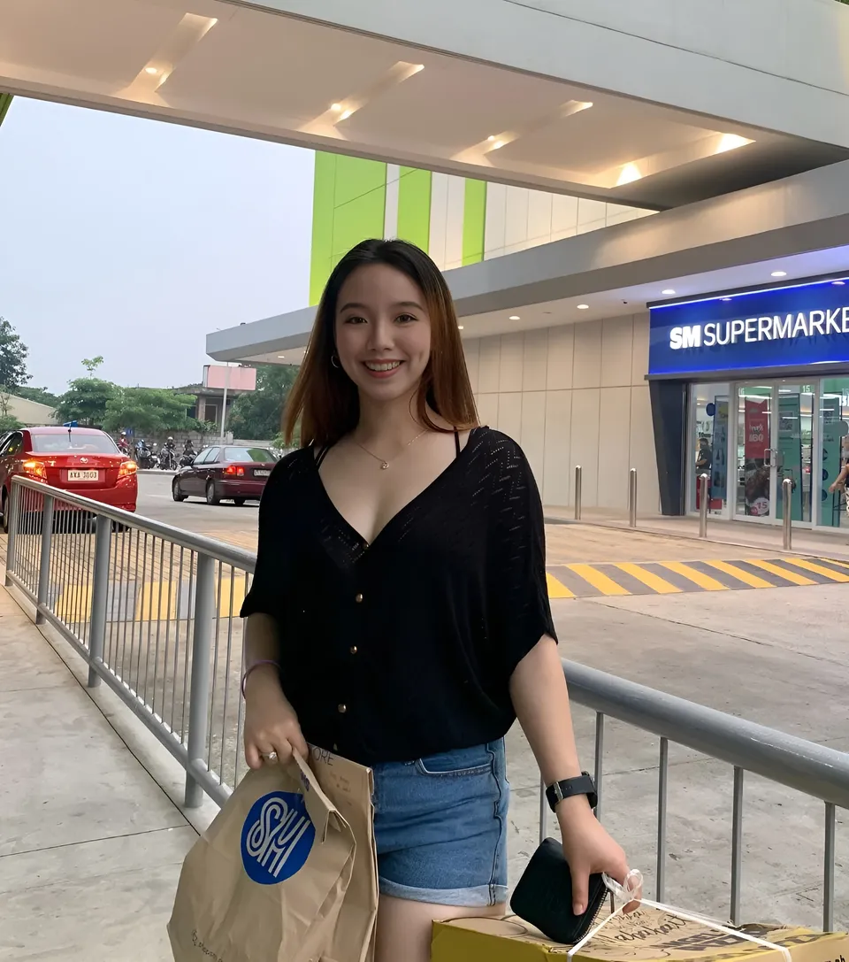Clairee Winslow in black top and denim shorts stands outside supermarket