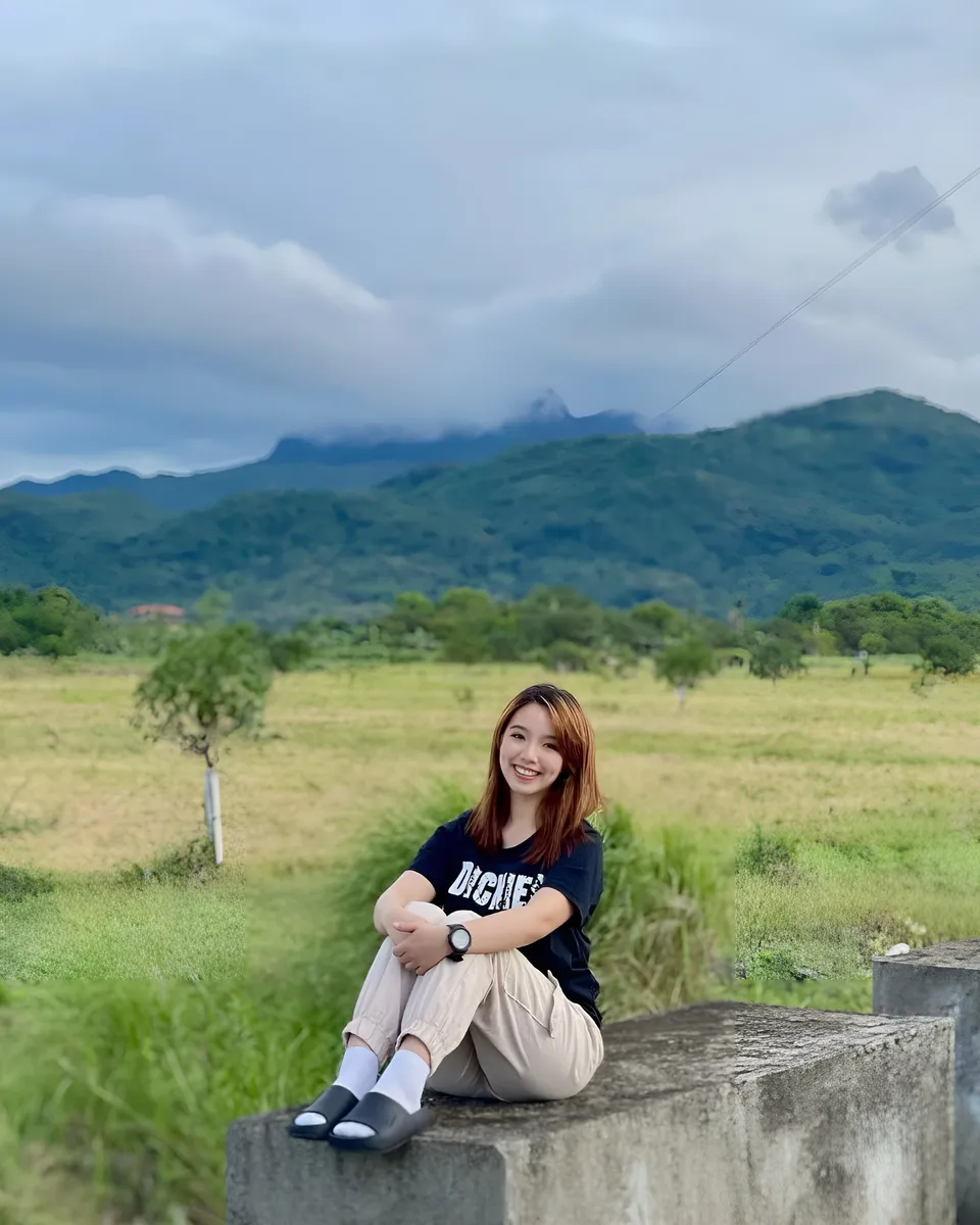 Clairee Winslow sits on concrete block in grassy field with mountains in background