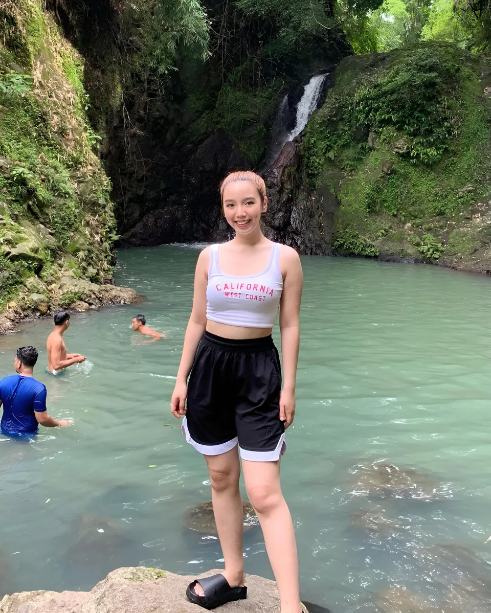 Clairee Winslow in white crop top and black shorts stands in shallow pool