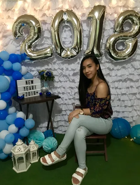 Dahnie Cia wearing a floral top and light jeans sits beside blue and silver balloons