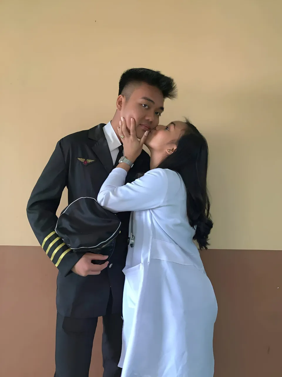 Dahnie Cia — Two people wearing a dark uniform and a white coat embrace indoors