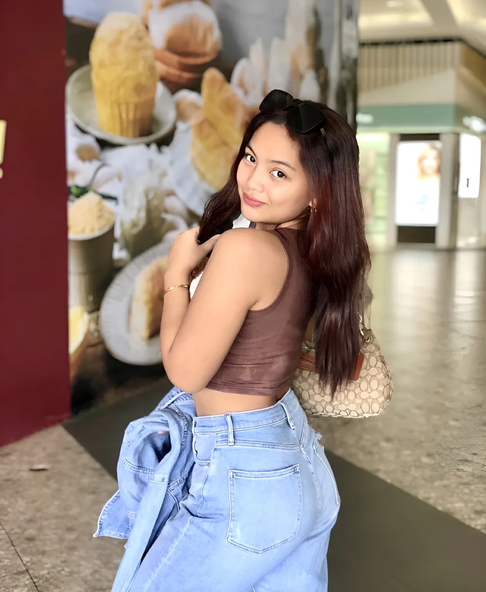 Daisy Monroe in brown top and jeans stands in mall with food mural behind