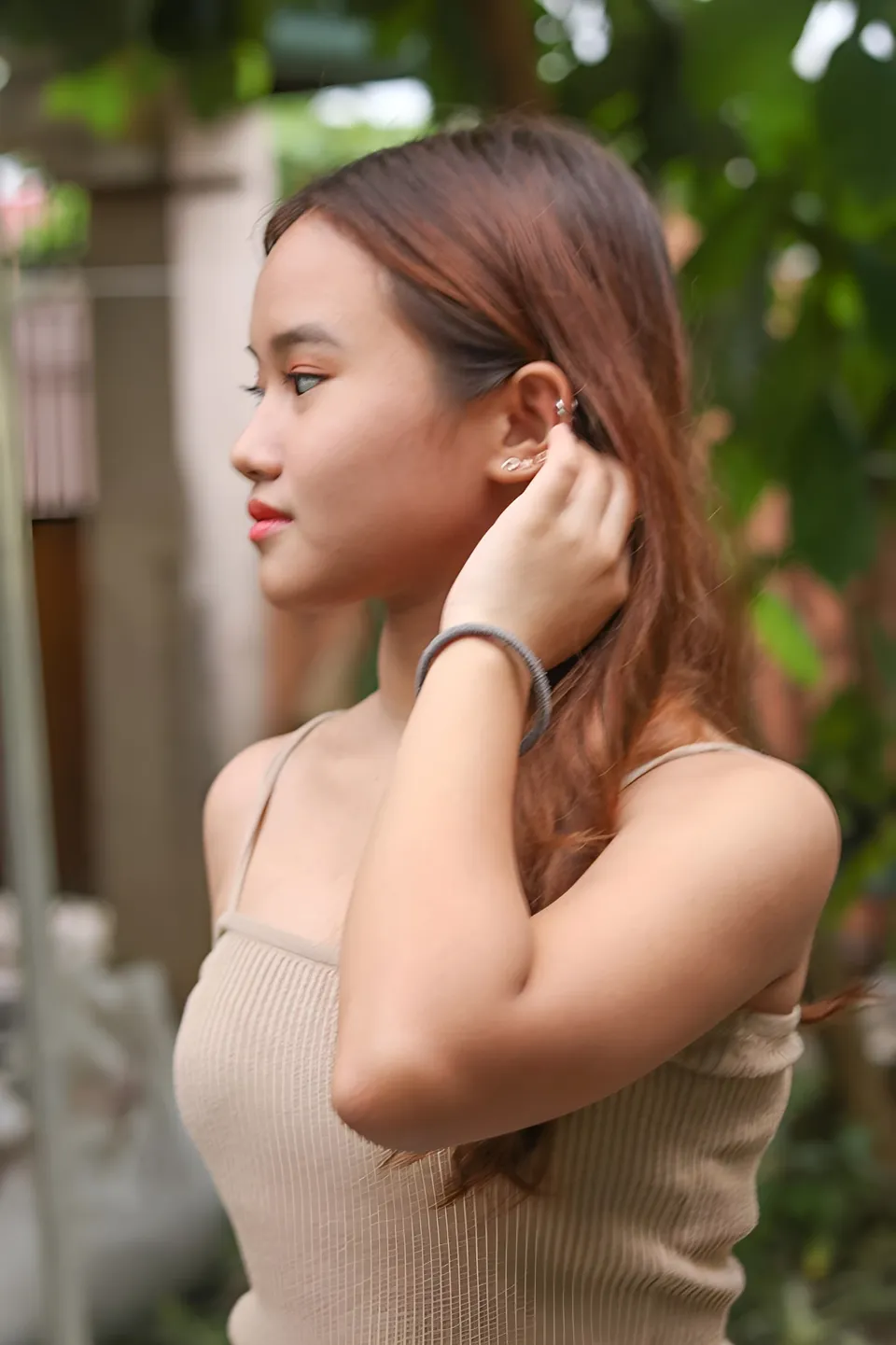 Elhaiza Maltao in beige top adjusting ear with hand outdoors