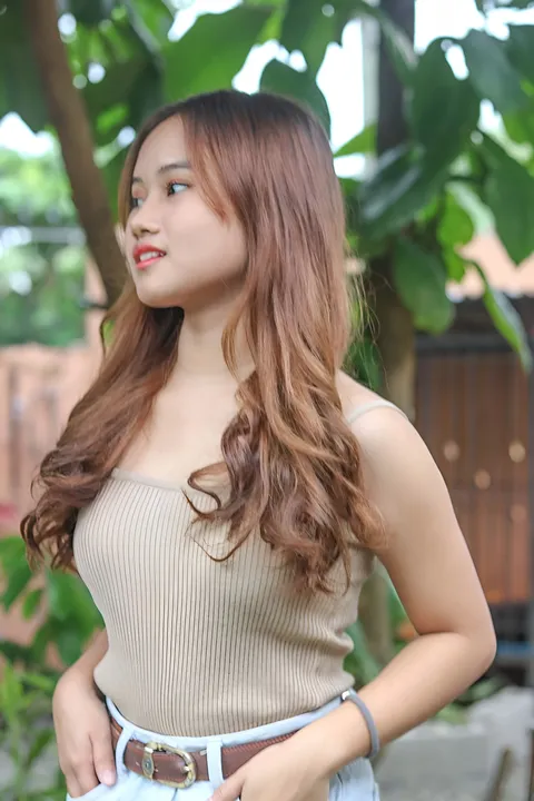 Elhaiza Maltao wearing a beige ribbed top poses outdoors near green foliage