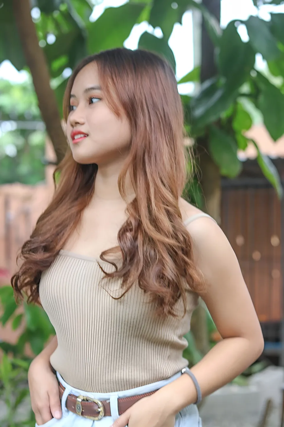 Elhaiza Maltao wearing a beige ribbed top poses outdoors near green foliage