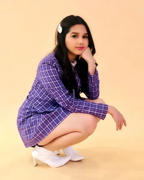 Elijah Alejo in purple plaid dress crouching on plain background