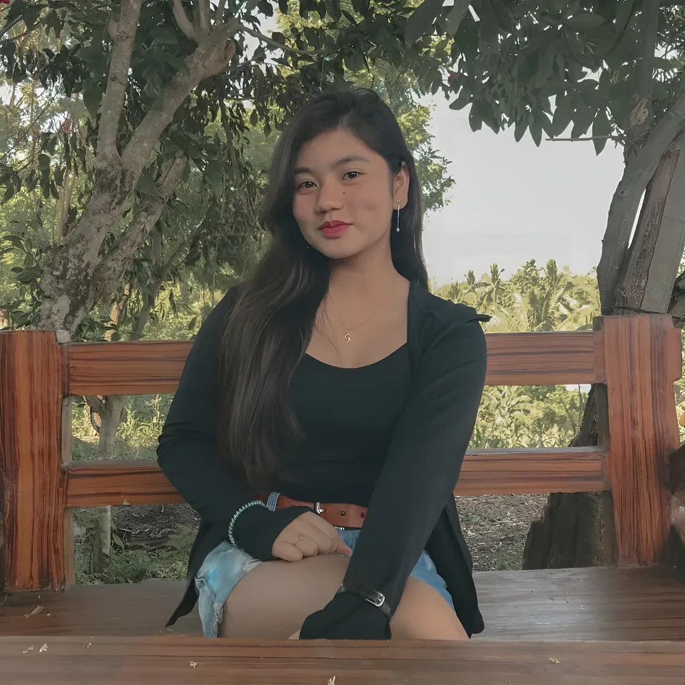 Ellidiethe Rielle seated on wooden bench outdoors under trees