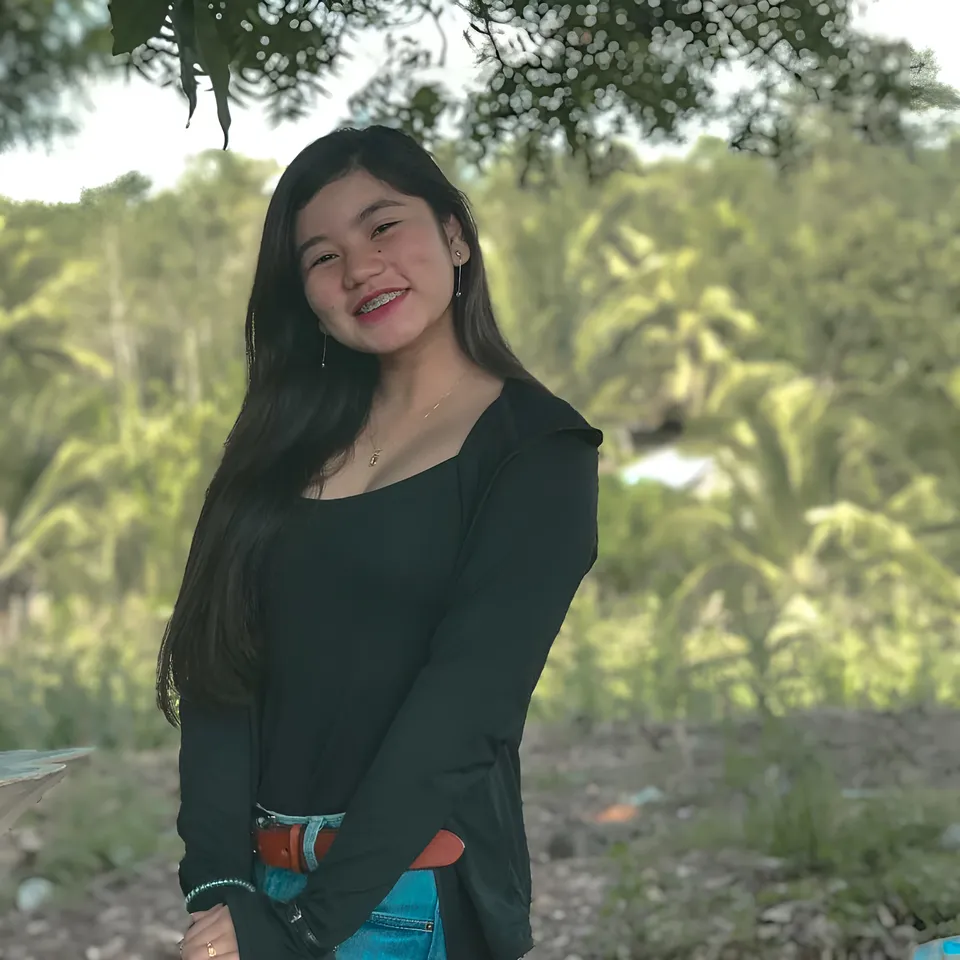 Ellidiethe Rielle in black top and jeans standing outdoors under tree