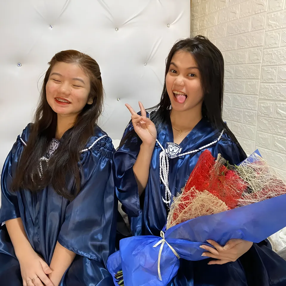 Ellidiethe Rielle — Two people wearing blue gowns sit together with flowers