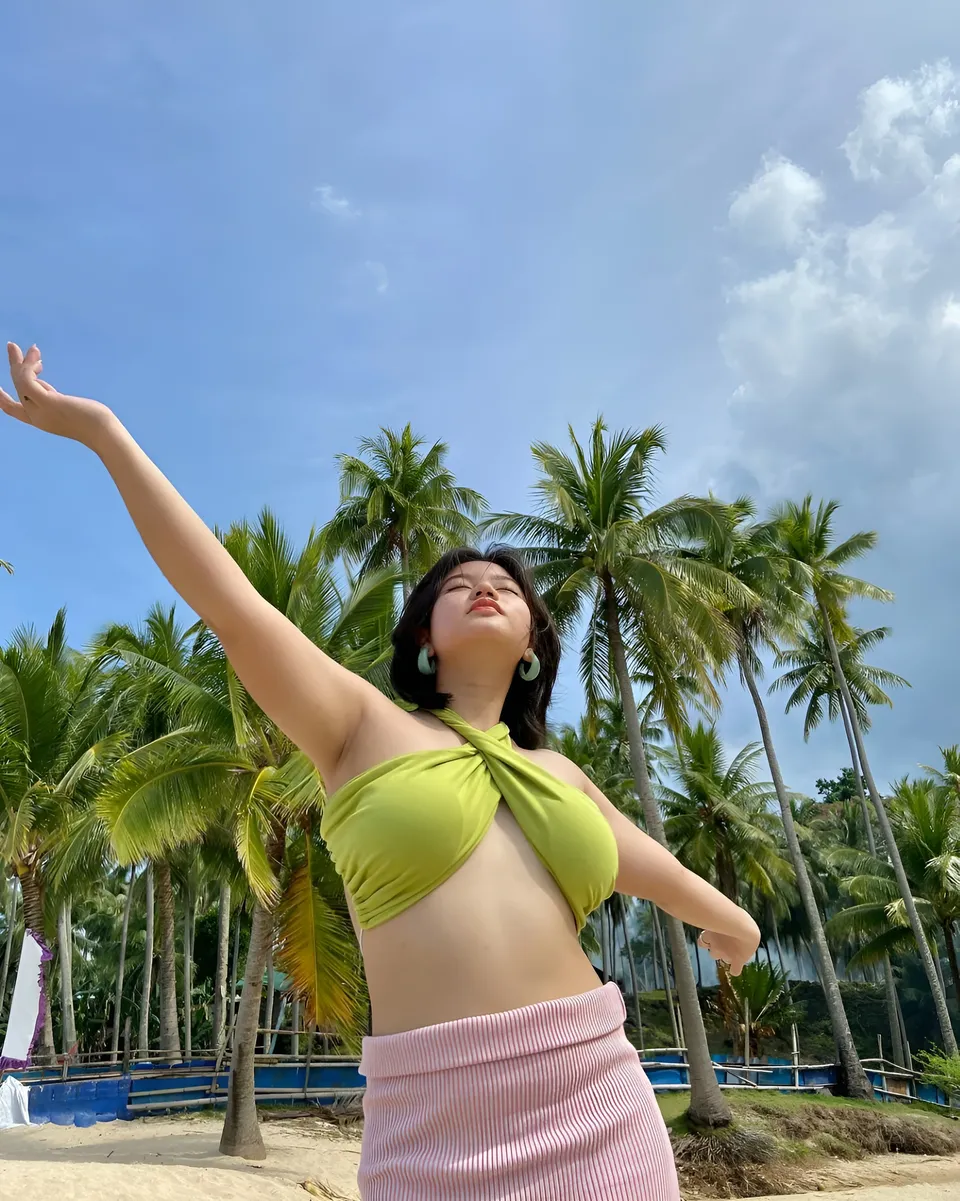 Ellidiethe Rielle in green top and pink skirt on beach with palm trees