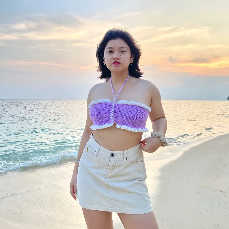 Ellidiethe Rielle stands on beach wearing purple crochet top and beige skirt