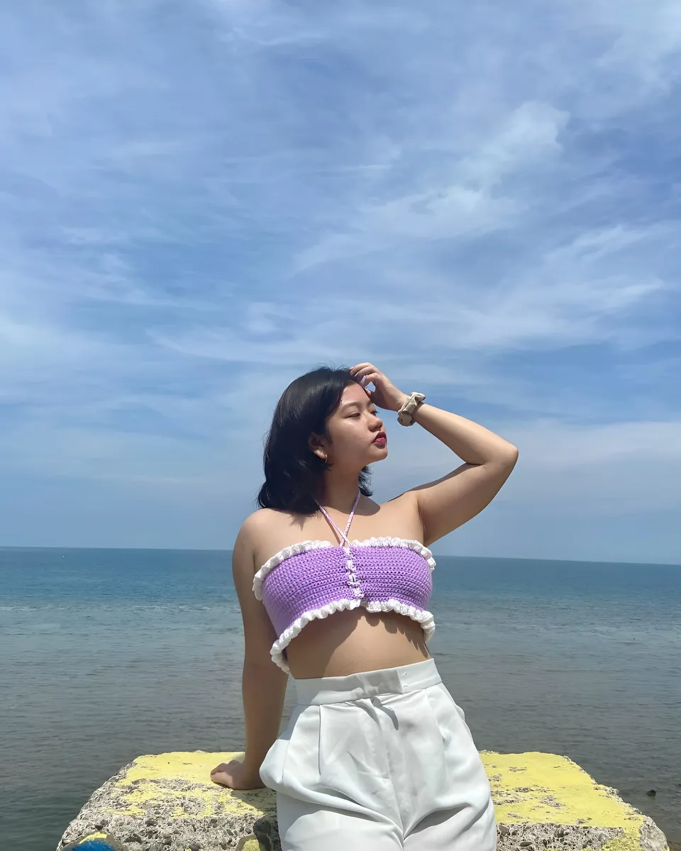 Ellidiethe Rielle in purple top and white pants stands by ocean