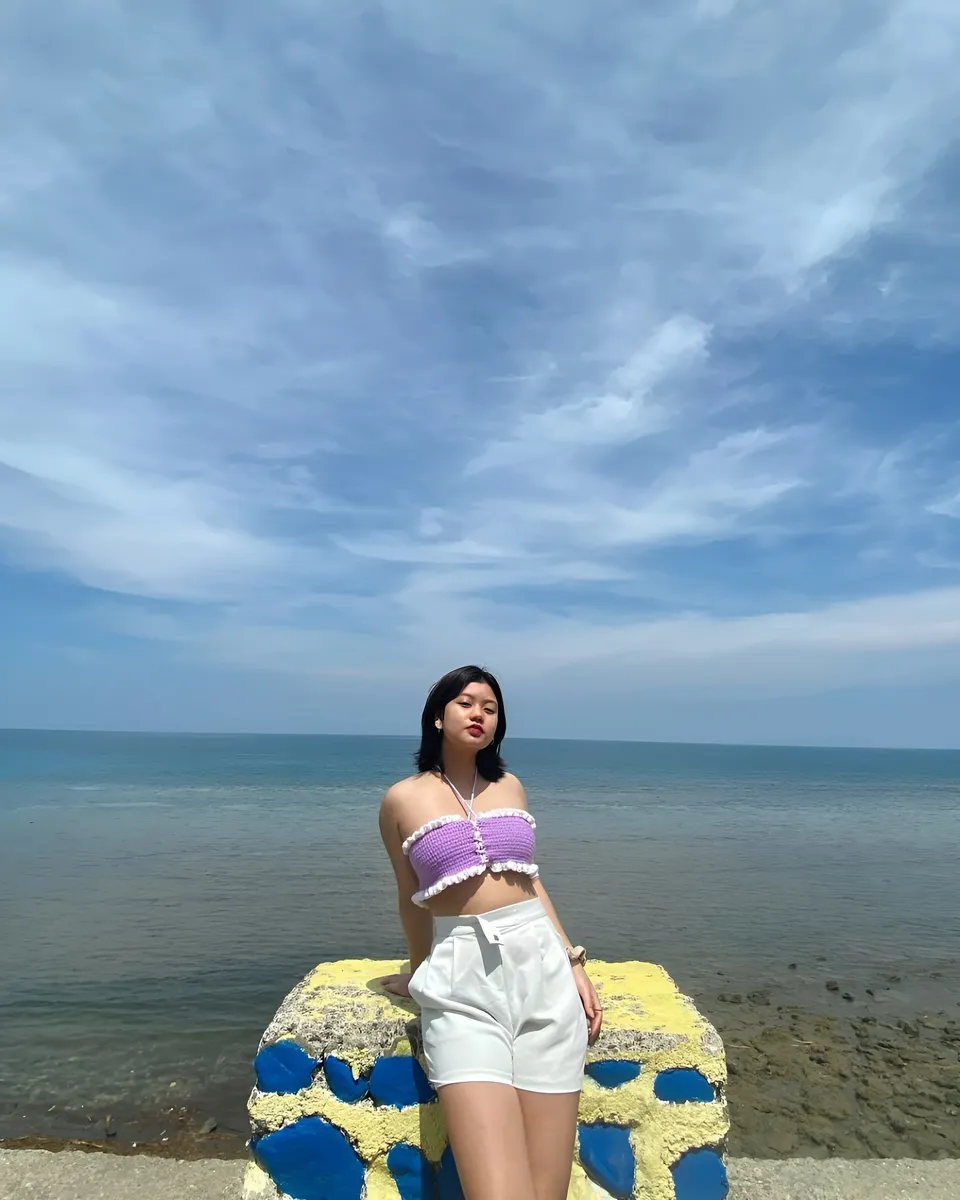 Ellidiethe Rielle in purple top and white shorts stands by colorful seaside structure