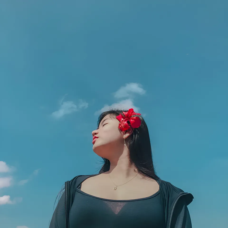 Ellidiethe Rielle with a red flower in their hair tilts their head against a blue sky