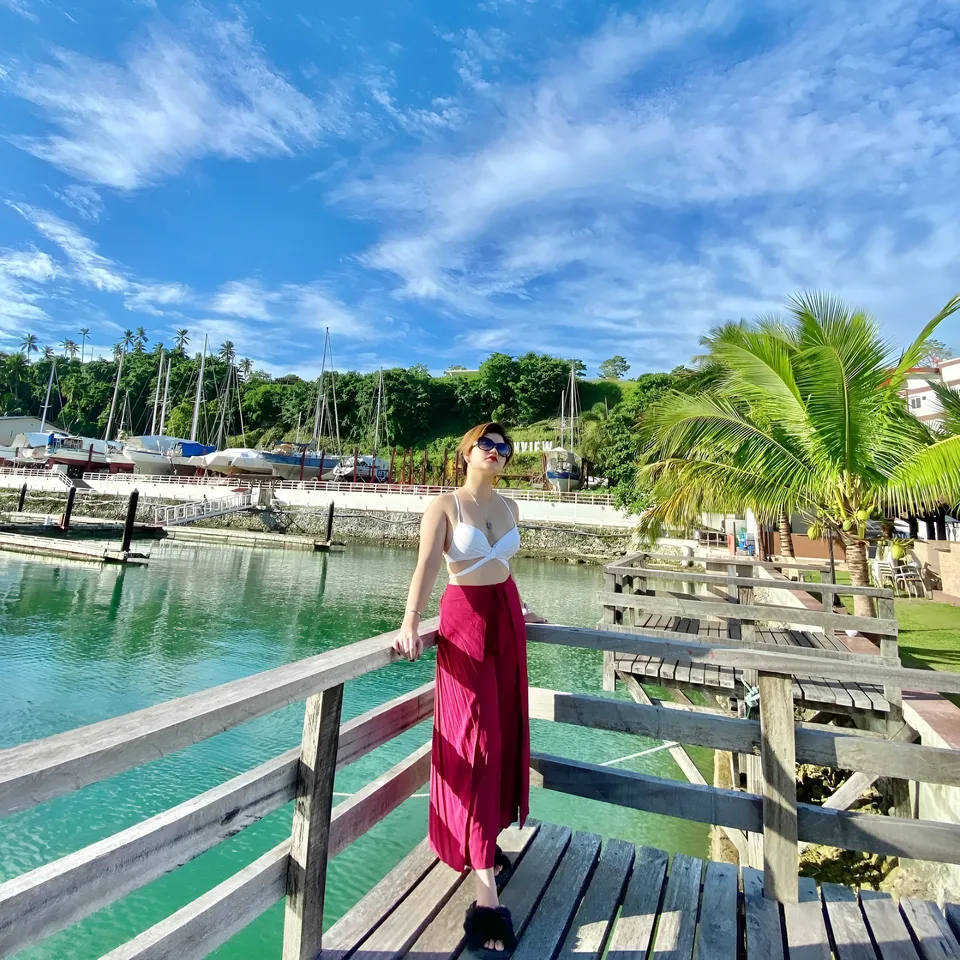 Ellidiethe Rielle in white top and red skirt stands on wooden dock near water