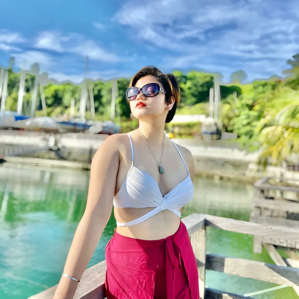 Ellidiethe Rielle in white top and red wrap stands by water