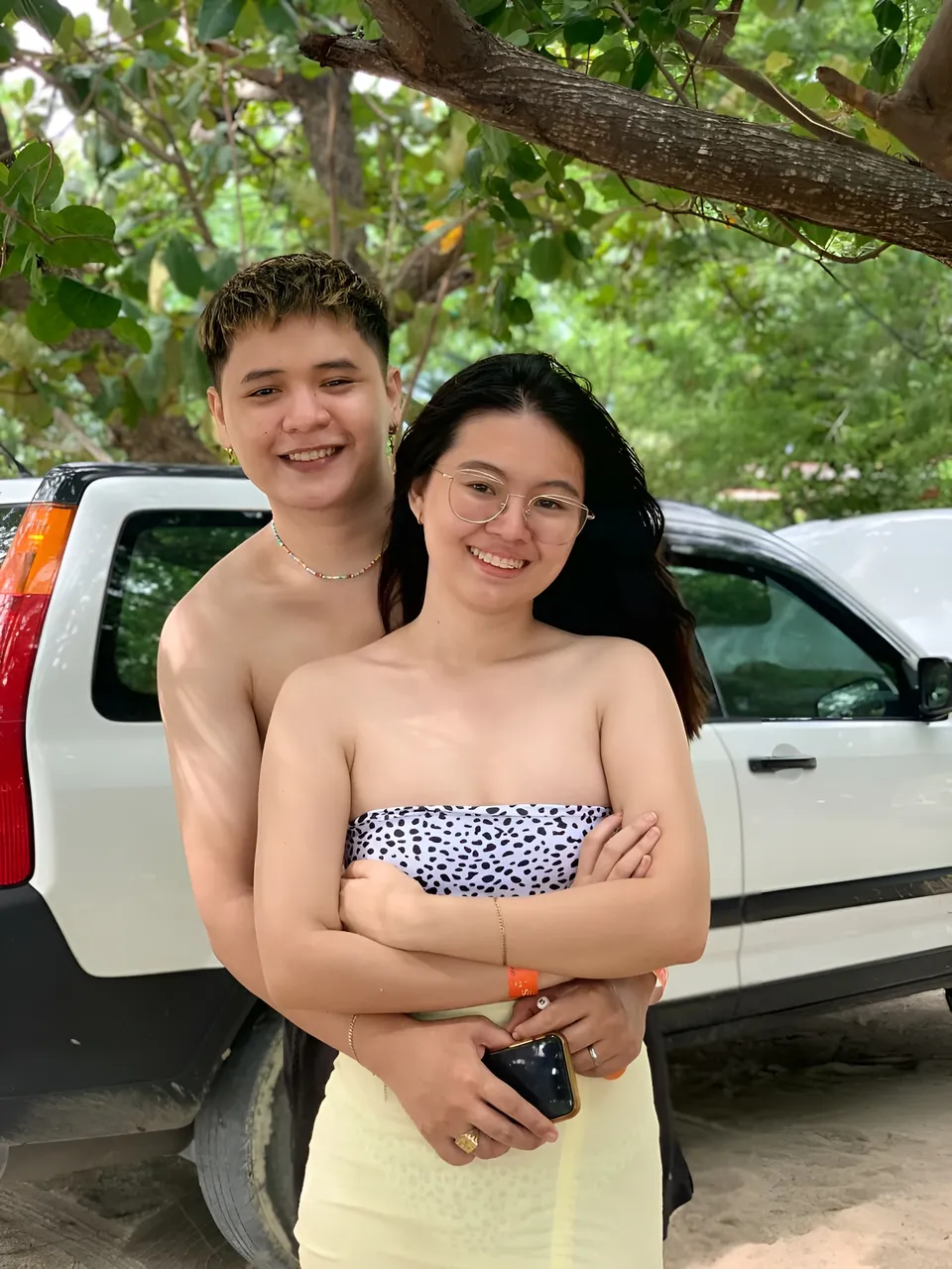 Erica Kyle — Two people embracing outdoors near vehicle under tree