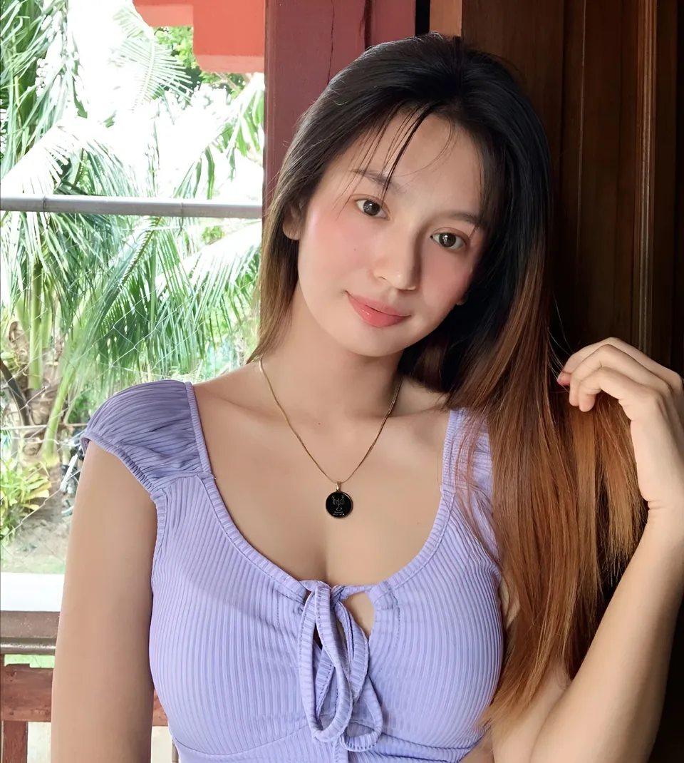 Eunice Lois in purple top with necklace, standing near window with plants