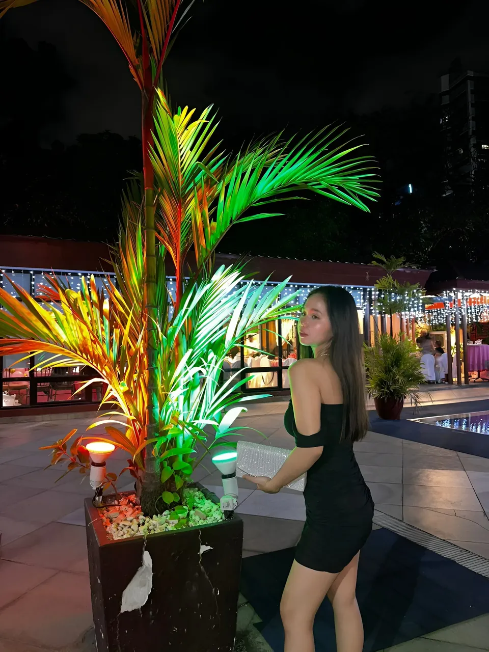 Faye Ramos in black dress stands beside illuminated plant at night