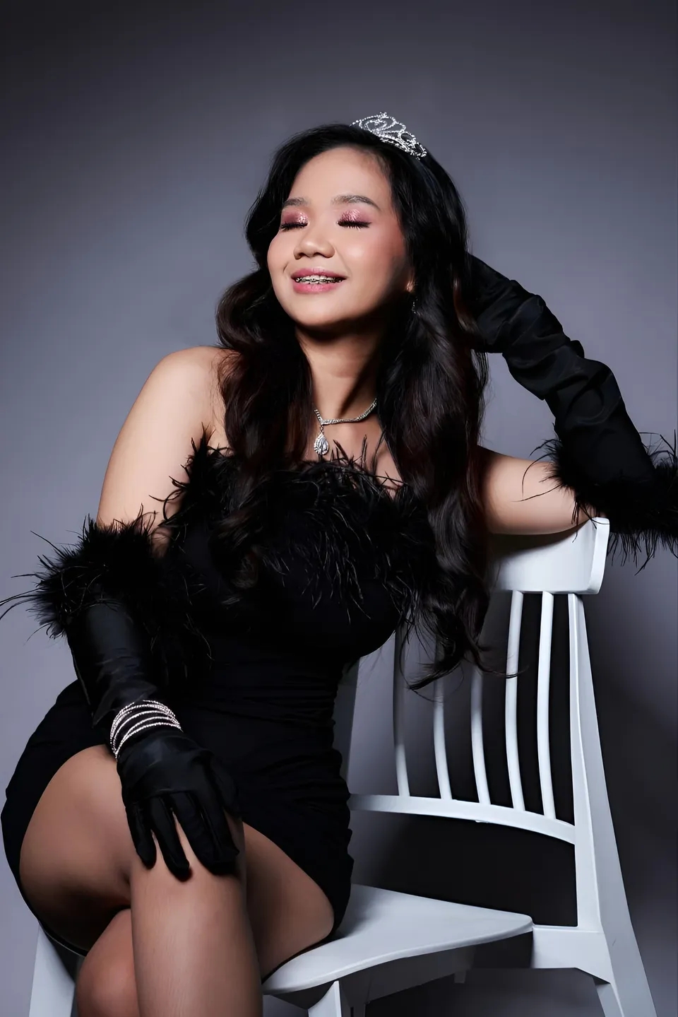 Faye Ramos in black feathered dress seated on white chair