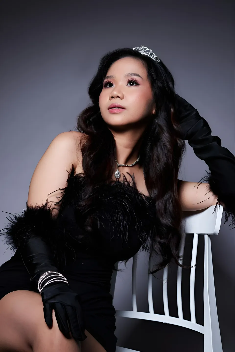 Faye Ramos in black feathered top seated on white chair