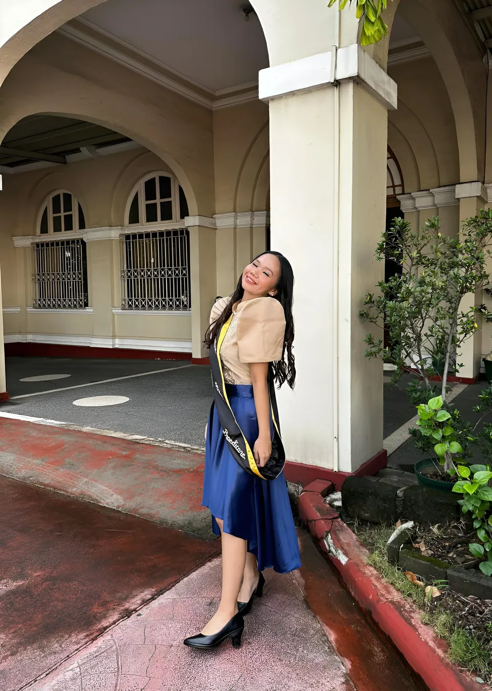 Faye Ramos in blue skirt and beige top stands outdoors near building