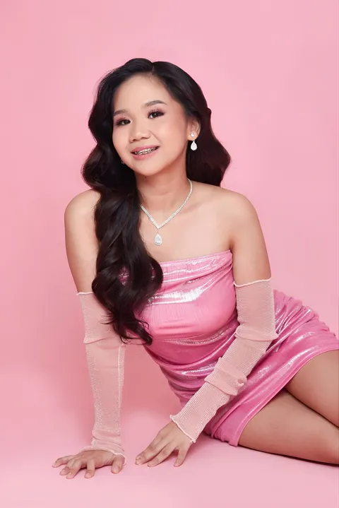 Faye Ramos in pink dress seated on pink surface