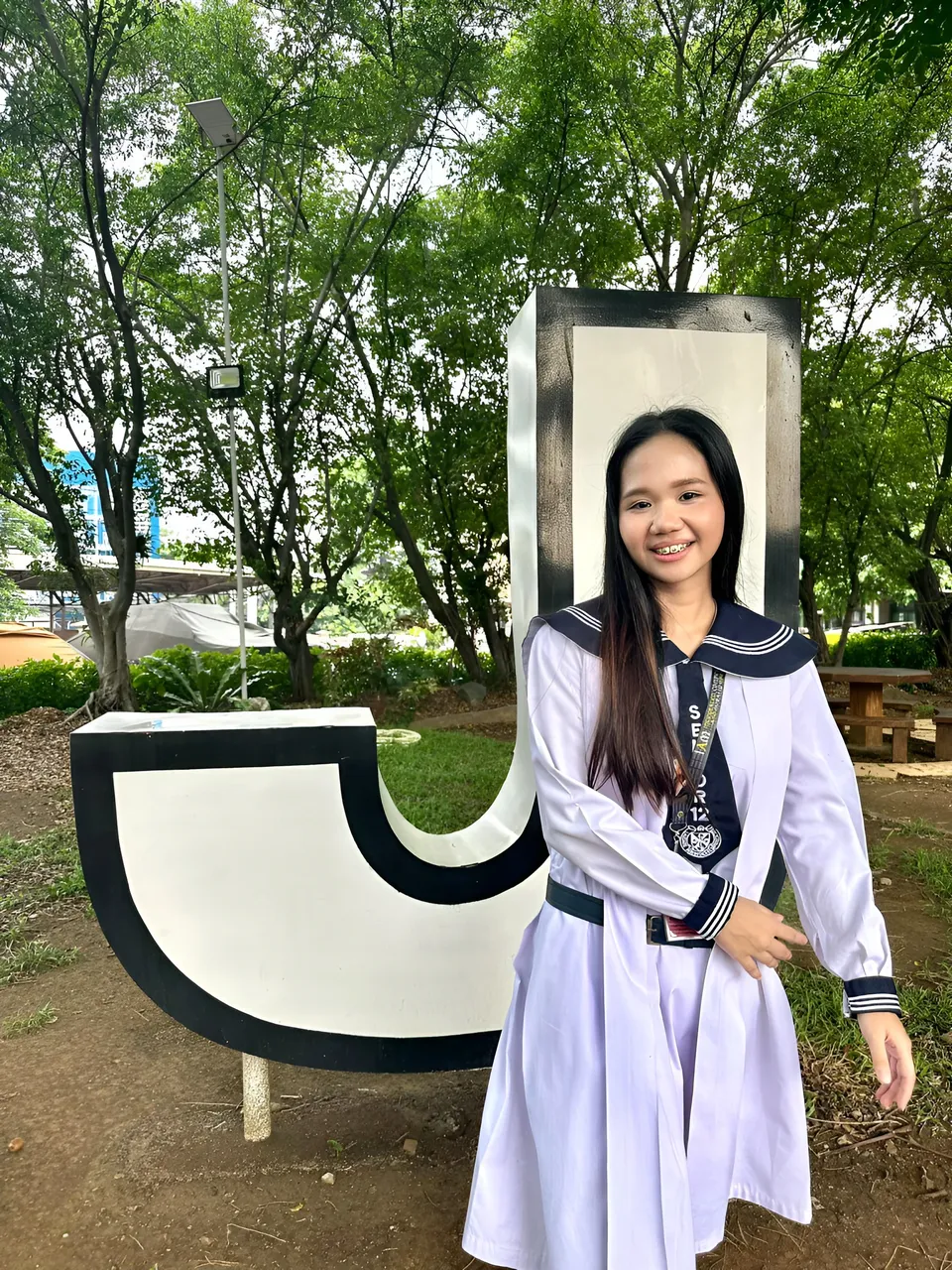 Faye Ramos in white sailor dress stands beside large letter sculpture outdoors