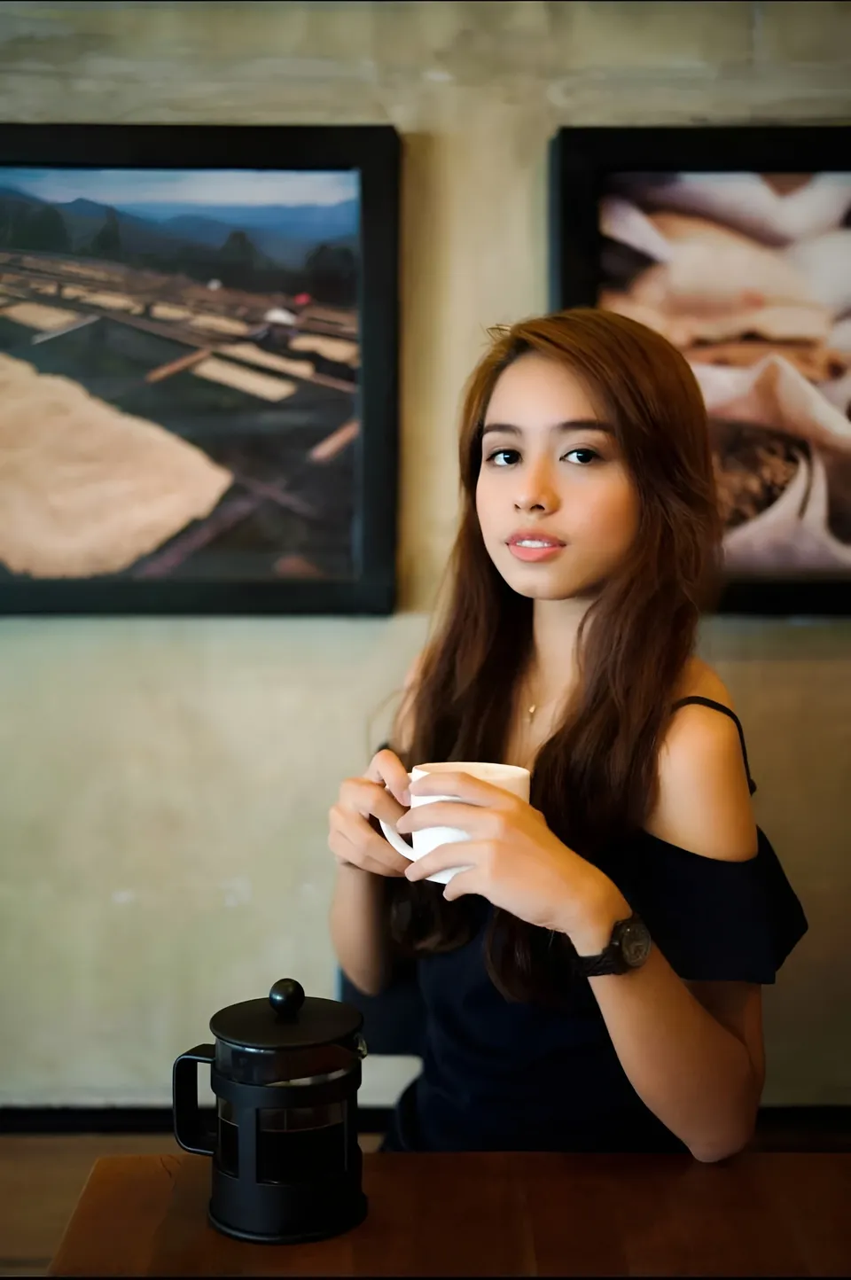 Francesca Ysabelle wearing a black top holds a white cup at a table