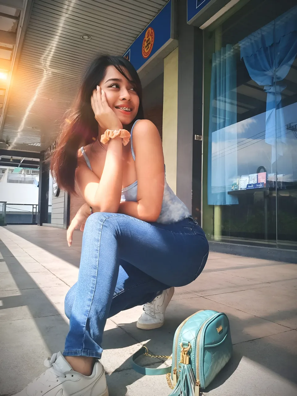 Francesca Ysabelle crouching on sidewalk near storefront with hand near face