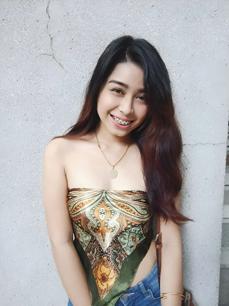 Francesca Ysabelle wearing patterned top and jeans standing against wall