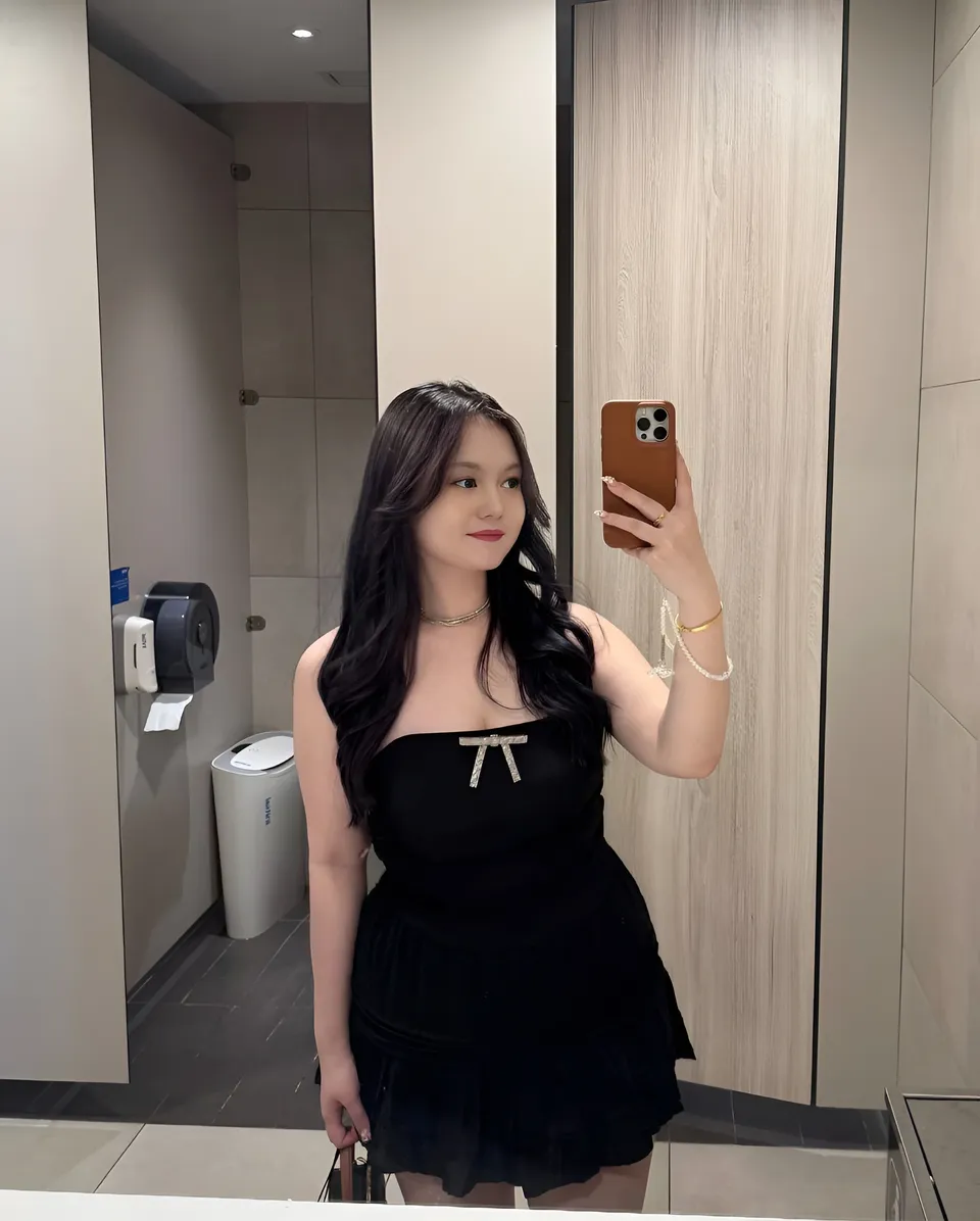 Gigi Laurent in black dress taking mirror selfie with phone