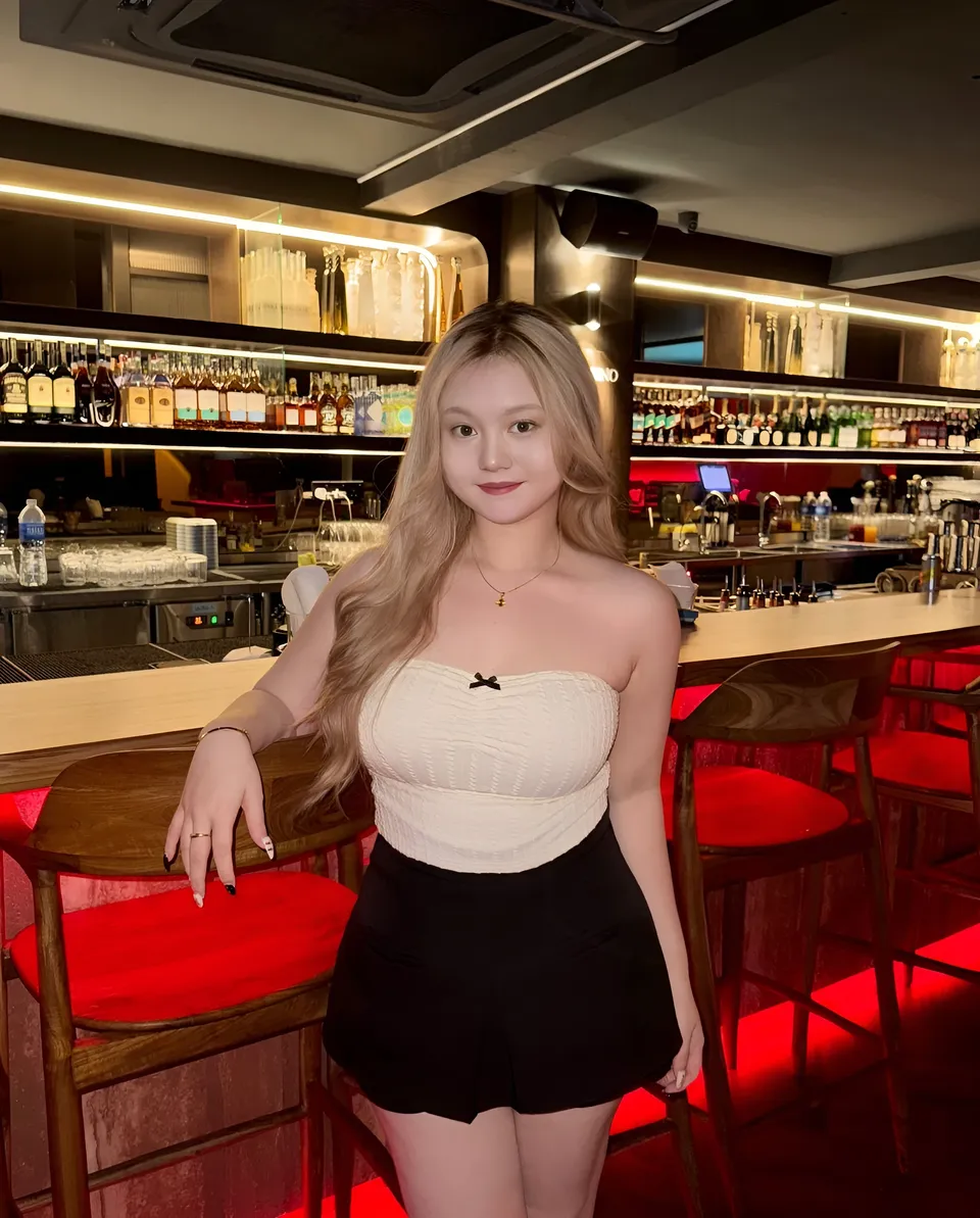 Gigi Laurent in white top and black skirt seated at bar