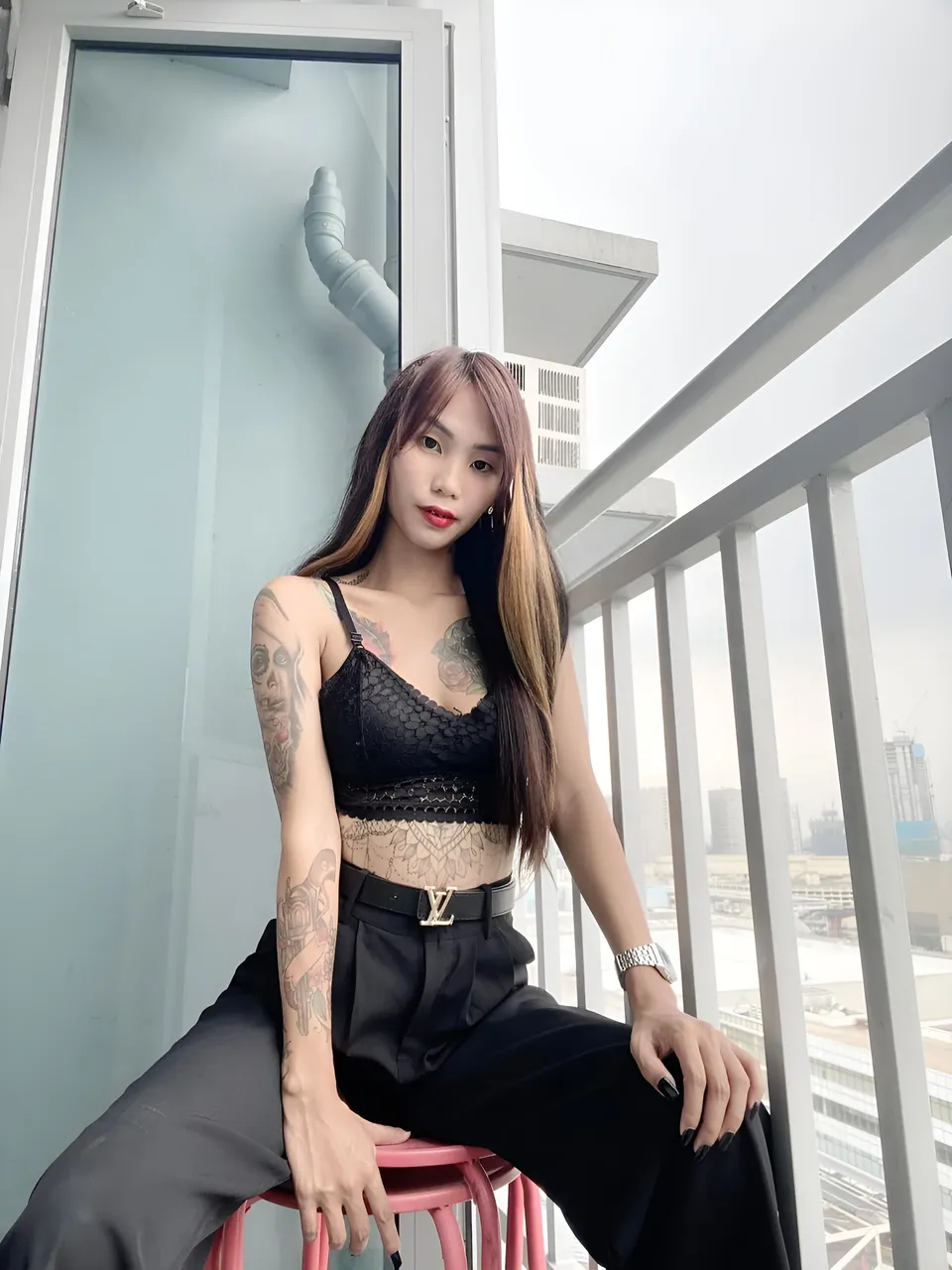 Gleiza Mercer in black lace top and pants seated on pink stool