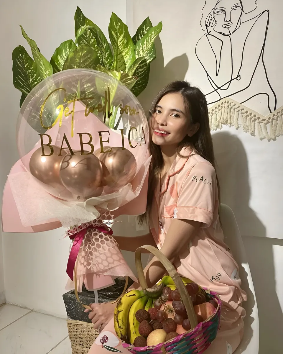 Ica Caparas in pink pajamas holds fruit basket and balloon bouquet