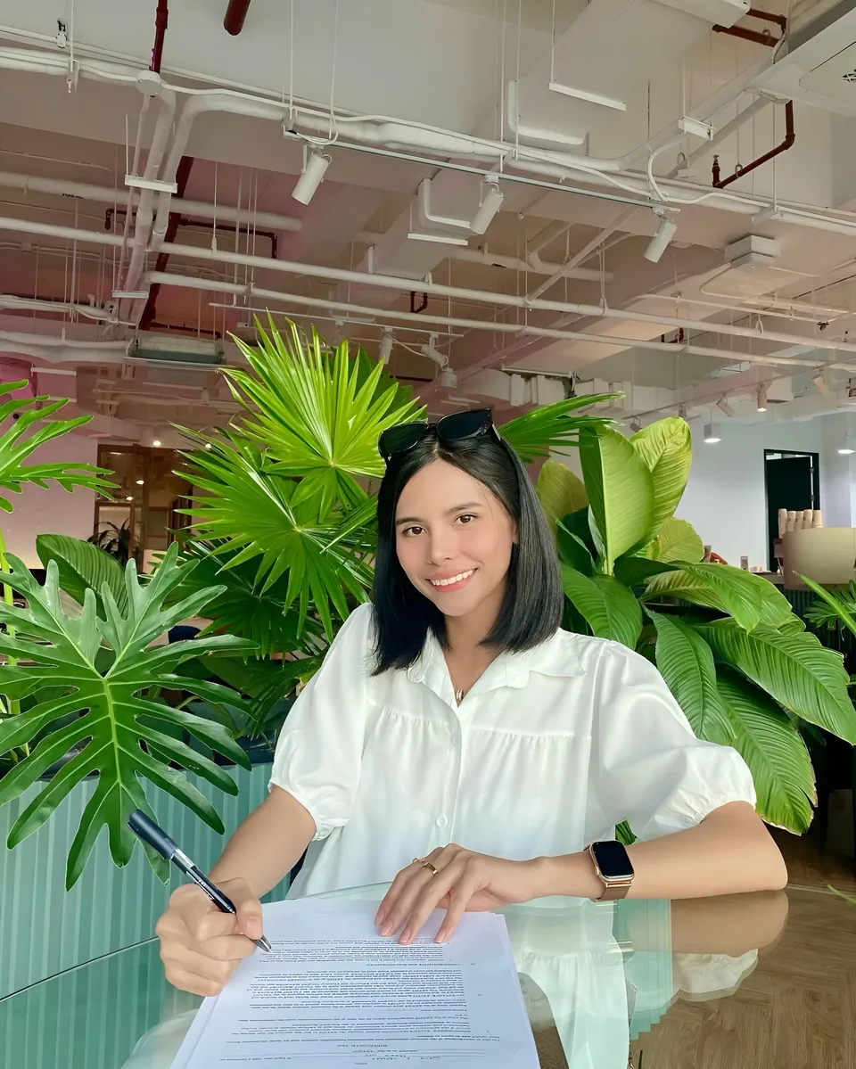 Ica Caparas in white blouse signing document at glass table