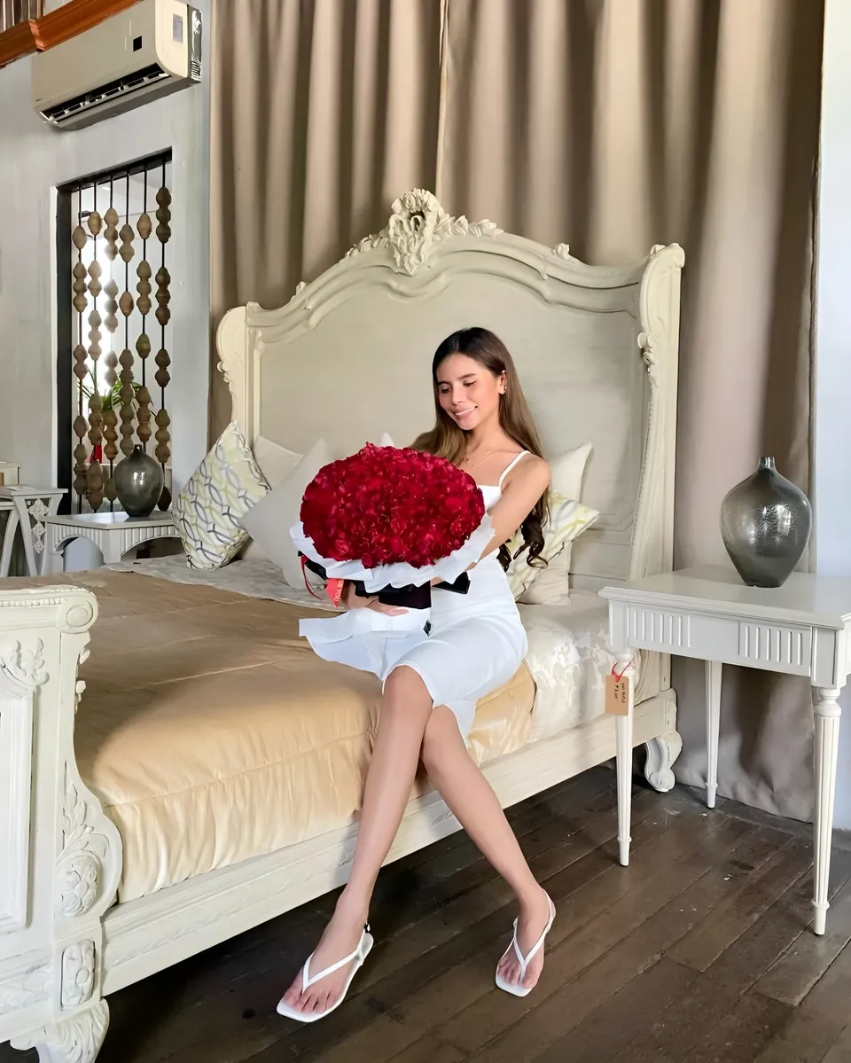 Ica Caparas in white dress holding red roses on bed