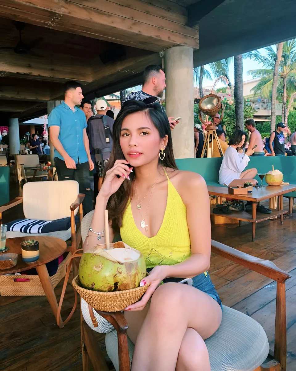 Ica Caparas in yellow top holding coconut at outdoor cafe