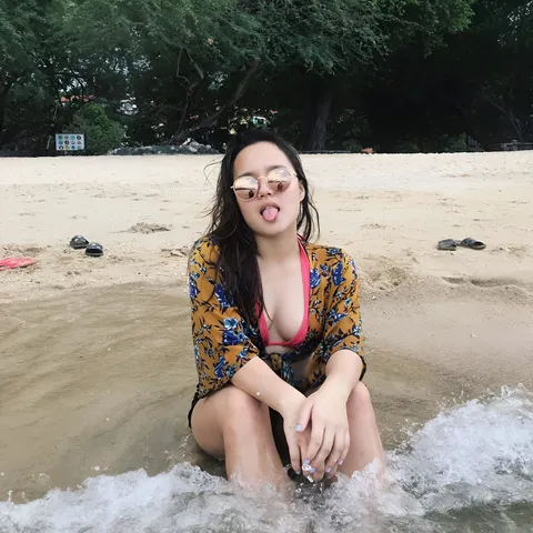Isla Abad Santos in floral top sitting in shallow water at beach