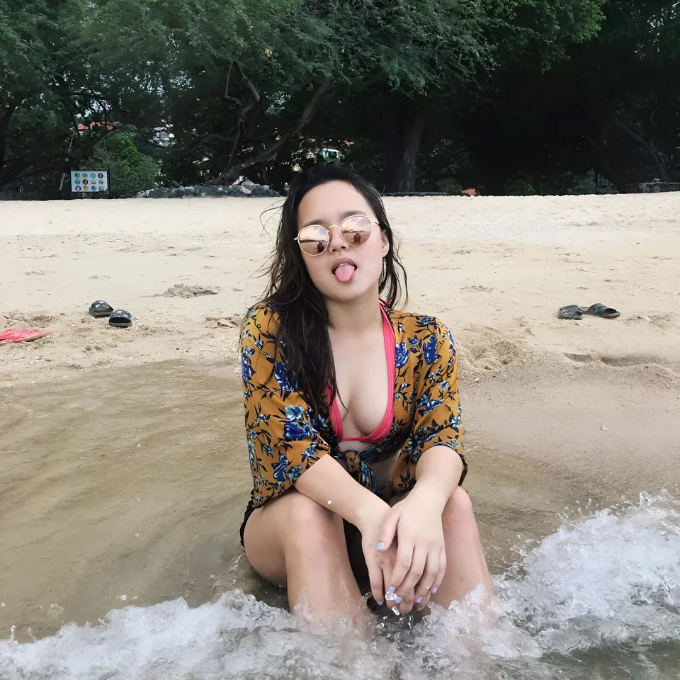 Isla Abad Santos in floral top sitting in shallow water at beach