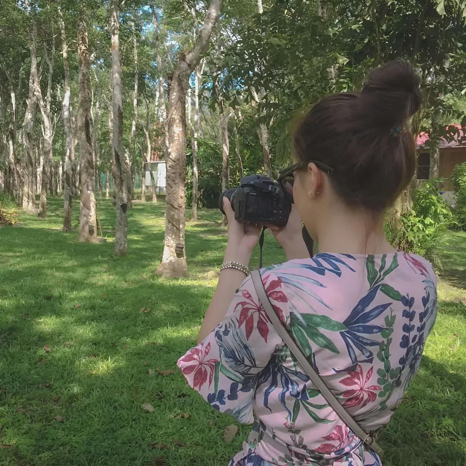 Jainbre Morgan in floral dress holding camera outdoors among trees