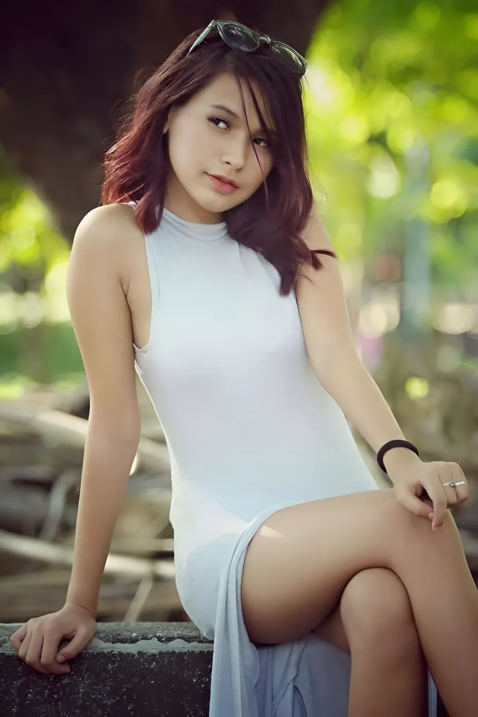 Jam Villanueva in a sleeveless white dress sits outdoors with sunglasses on their head