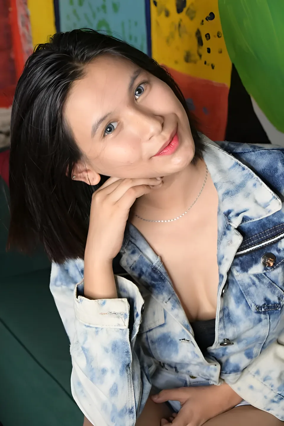 Jamie Arden in a denim jacket rests their chin on one hand beside a colorful backdrop