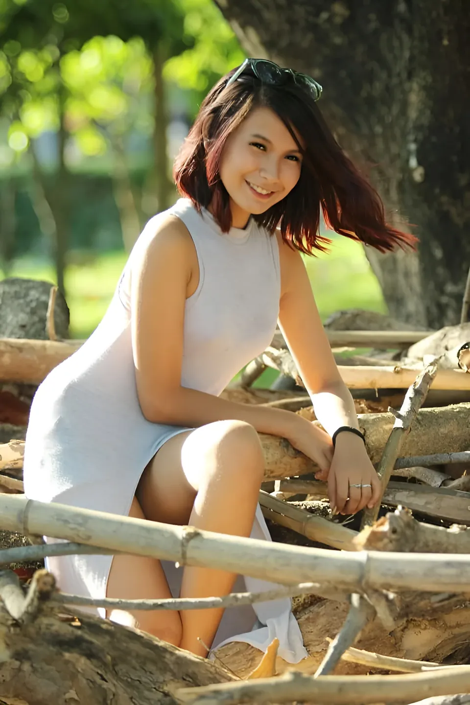 Jamie Arden in a sleeveless white dress sits among branches against a green background