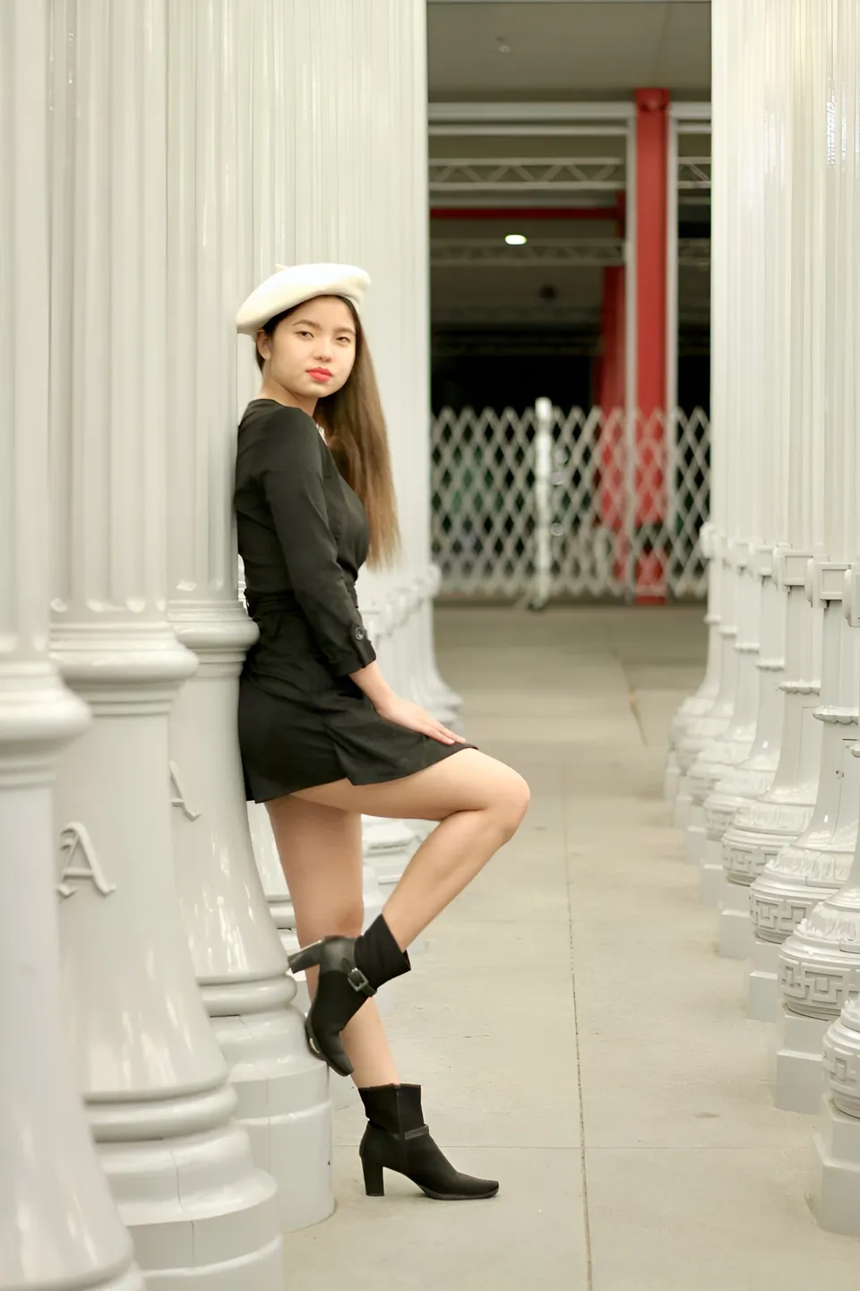 Jann Tiffany Mendoza wearing a black dress and white hat poses among white columns