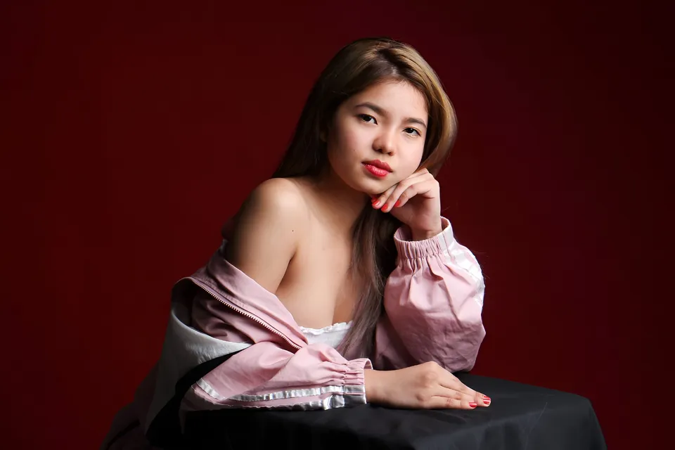 Jann Tiffany Mendoza in pink jacket resting chin on hand against red background