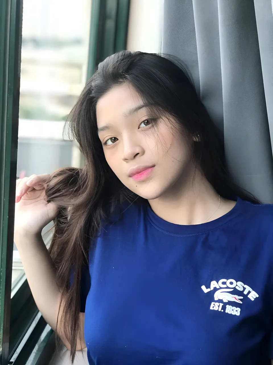 Jaymie Vale wearing a blue shirt poses beside a window
