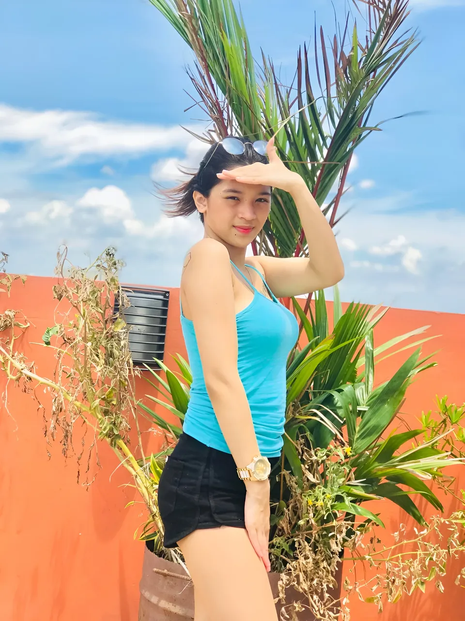 Jaymie Vale in blue top and black shorts standing outdoors with palm plants